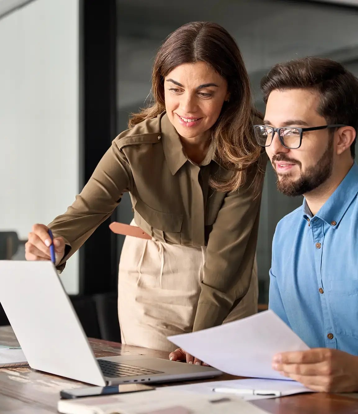 Woman helping male colleague with reviewing document on laptop
